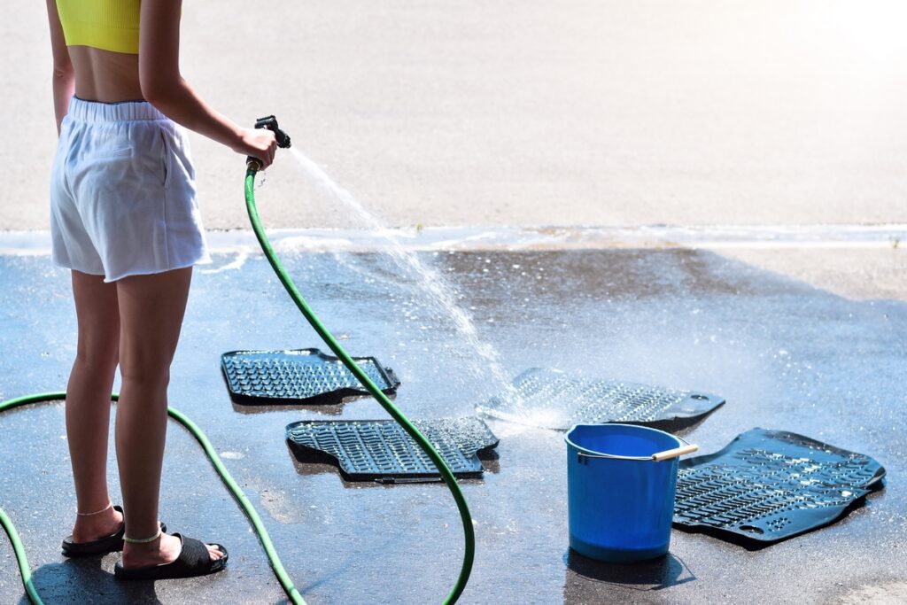 Young girl washing car mats on a driveway